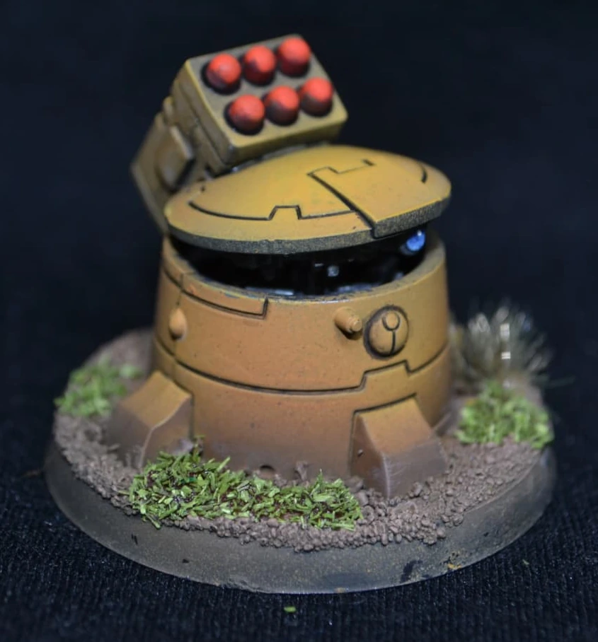 Tau Geschütz in gelbem Farbschema mit roten Raketen und blauem Sensor auf begrünter Base